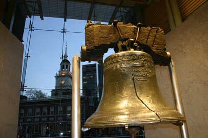 The Liberty Bell with its crack, seen through glass, with Independence Hall in background.