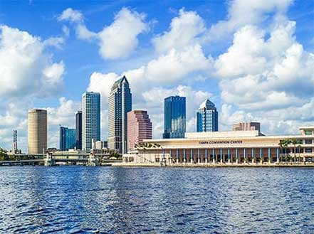 Tampa skyline with modern skyscrapers reflecting in the Hillsborough River under a blue sky.